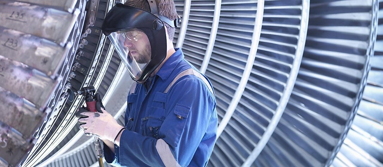 Engineer repairing steam turbine blade with grinder in workshop
